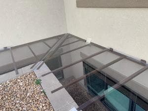 Glass canopy installation over a modern building entrance with gravel landscaping.