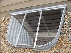 Basement window well cover with mesh screen and metal frame over gravel landscaping.