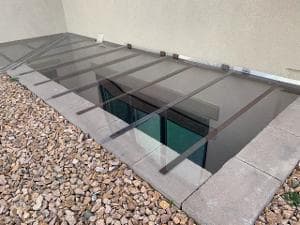 Glass walkway cover over gravel landscape with metal supports and interior visibility.
