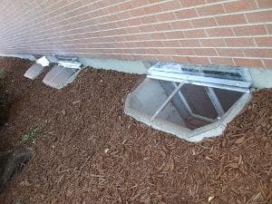 Basement window wells with gravel landscaping next to a brick wall.