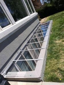 Window well with protective cover installed next to a house on a grassy lawn.