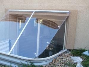 A clear window well cover mounted on a house, protecting the basement from debris and water.