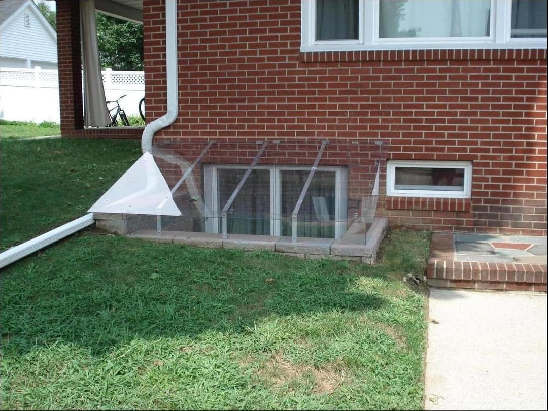 Window well with clear cover on a brick house, surrounded by grass, enhancing basement light.