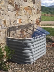 Compost bin with a clear lid next to a stone wall in a landscaped outdoor setting.