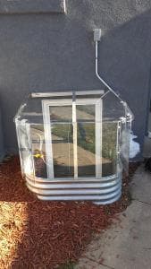 Clear outdoor greenhouse with metal frame and vent, designed for gardening and plant growth.