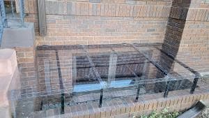 Glass window well cover on brick building exterior for safety and protection.