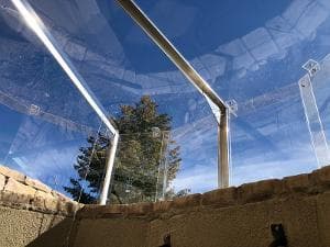 View from below a glass structure, showing clear panels and blue sky overhead.