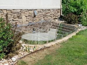 Garden greenhouse with glass panels and stone foundation, surrounded by lush greenery.